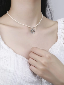 Detail of a dainty daisy pendant on a pearl necklace worn with a white lace shirt