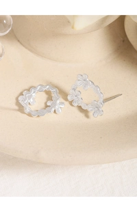 Detailed view of asymmetric silver floral earrings on a textured ceramic tray