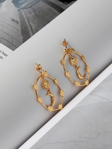 Detailed close-up of 18K gold star and moon drop earrings with bohemian sun face carvings