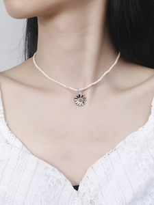 Detail of a dainty natural pearl necklace featuring a silver daisy pendant on a model