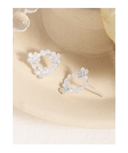 Macro shot of silver asymmetrical flower stud earrings on a cream ceramic plate