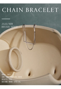 Artistic display of minimalist silver chain bracelet with sleek metal tubes on ceramic