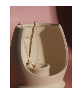 Detailed view of S925 silver necklace with white pearls and gold bead on ceramic
