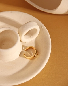 Detailed close-up of a minimalist gold layered ring on a white ceramic display stand