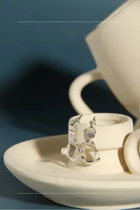 Detailed view of silver irregular liquid metal earrings with white pearls on a tray