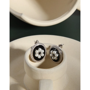 Macro view of vintage oval silver earrings with black glaze and pearl flower details