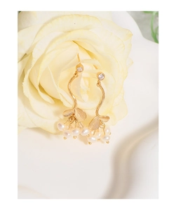 Détail de boucles d'oreilles branche dorée avec perles blanches sur une fleur jaune