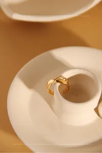 Detail of a minimalist gold crossover ring placed on a beige ceramic display tray