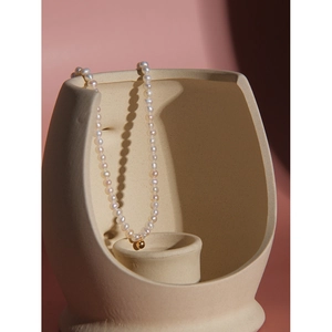 Minimalist S925 silver pearl necklace with a gold bead displayed on ceramic vessel