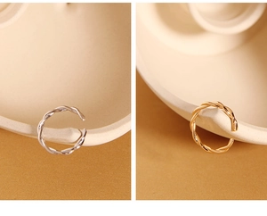 Detailed close-up showing twisted gold and silver minimalist open rings on ceramic background