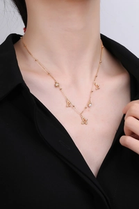 Nahaufnahme einer goldenen Schmetterlingskette mit Perle und Blumenanhänger am Model