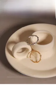 Detail of minimalist twisted rope rings in gold and silver finish on ceramic tray