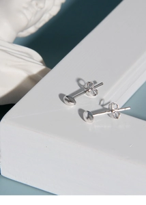 Close-up of minimalist S925 sterling silver bean stud earrings on a white geometric stand
