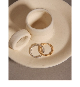 Detailed view of twisted rope rings in gold and silver finishes on a ceramic tray
