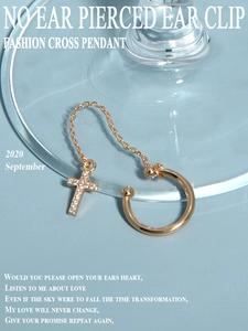 Detail of a gold cross chain ear cuff with white rhinestones on a blue background