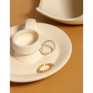 Detail of gold and silver beaded open rings on cream ceramic with warm aesthetic lighting
