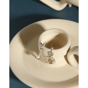 Detailed close-up of irregular silver hoop earrings with white pearls on ceramic edge
