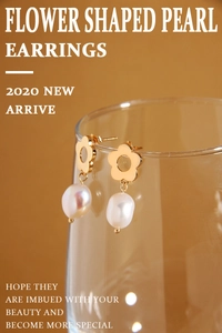Detail of gold hollow flower earrings with white baroque pearls on a glass rim