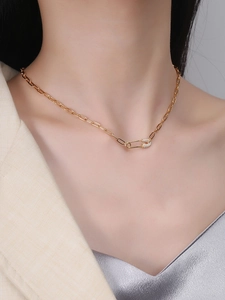 Macro detail of gold safety pin pendant with pavé crystals on paperclip chain