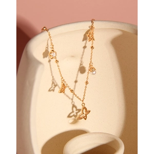 Elegante goldene Schmetterlingskette mit Perlen und Zirkonanhängern auf rosa Hintergrund