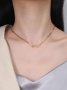 Detail of gold paperclip chain necklace with a zircon-encrusted safety pin pendant