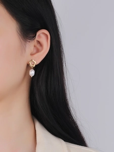 Close-up of elegant gold flower stud earrings with a dangling white oval pearl