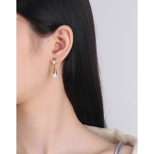 Elegant gold drop earrings with white teardrop pearls shown on a female model