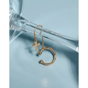 Detailed view of a gold cross chain ear cuff with zircon inlay on a glass edge