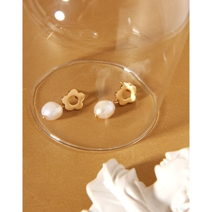 Detailed close-up of gold flower earrings with baroque pearls resting in a glass cup
