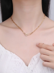 Detail of gold paperclip chain necklace with a zircon-encrusted safety pin pendant