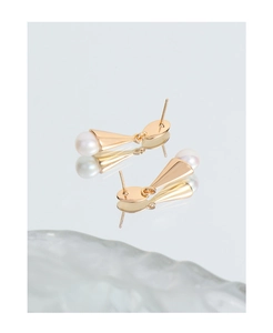 Detailed close-up of cone-shaped gold-plated silver earrings with white freshwater pearls