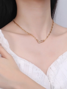 Detailed view of a gold safety pin necklace with micro-pave crystals on paperclip chain