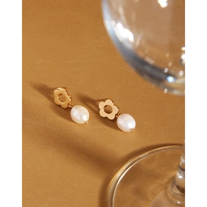 Detailed view of elegant gold flower earrings with white pearls on a warm aesthetic backdrop