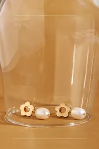 Detail of flower shaped gold earring with teardrop pearl inside a glass display case