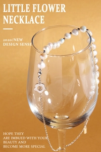 Detail of baroque pearl necklace with floral pendant draped over a glass on warm gold back