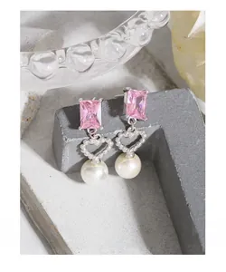 Detail of silver drop earrings with pink gems, heart charms and white pearls
