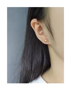 Detailed close-up of a gold safety pin earring with sparkling crystals and a white pearl
