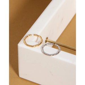 Dettaglio di anelli aperti a treccia oro e argento su supporto in marmo con luce naturale