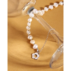 Macro detail of asymmetric pearl necklace with silver flower pendant on sandy background