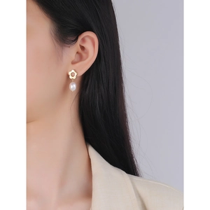 Elegant gold flower stud earrings with hanging white pearl on model profile view