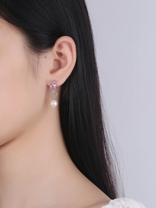 Close-up of pink zircon and pearl heart earrings worn on ear with soft lighting