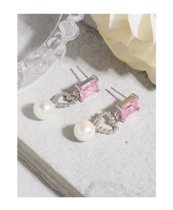 Detailed close-up of pink zircon and white pearl stud earrings on a gray stone surface