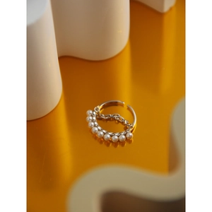 Macro shot of silver ring featuring white pearls and fine chain on yellow reflective base