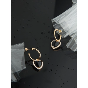 Close-up of heart-shaped gold earrings with black agate and sparkling diamond accents