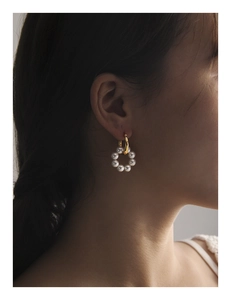 Détail de boucles d'oreilles créoles dorées avec perles blanches portées par un mannequin