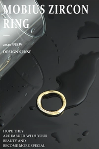 Détail d'une bague Möbius plaquée or avec zircons sur un fond miroir noir avec des gouttes d'eau
