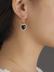 Close-up of heart-shaped black onyx earrings with white diamonds on golden hoops