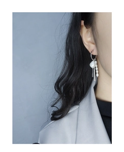 Detail of silver tassel earring with baroque pearl and zircon chain on female model