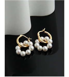 Détail de boucles d'oreilles dorées avec perles blanches sur surface miroir contrastée