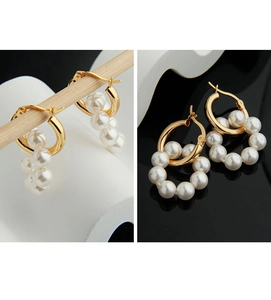 Détail de boucles d'oreilles créoles dorées avec perles blanches sur un support en bois
